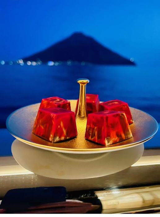 Rote Gelée-Würfel auf goldenem Teller vor Abendkulisse